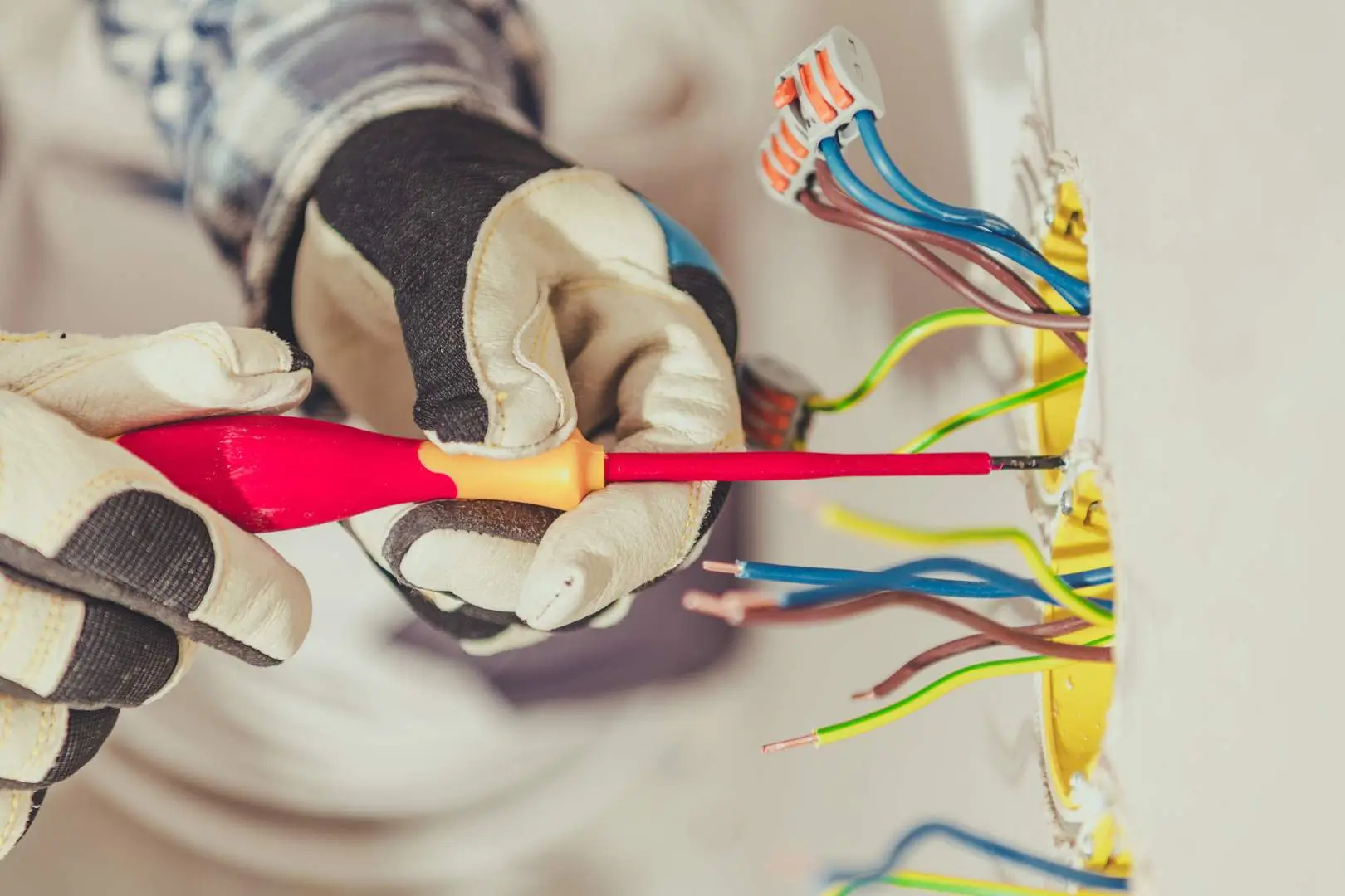 Electrician – Sydney CBD – tradesperson securing wall wiring using an insulated screwdriver and safety gloves.