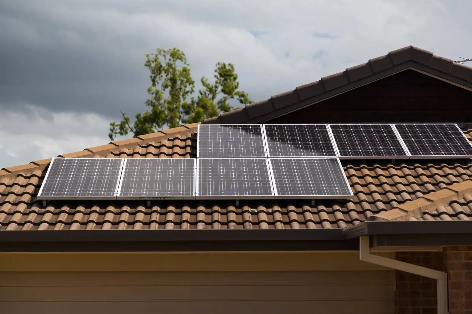 Solar panels installed in rows on a tiled residential roof under an overcast sky.