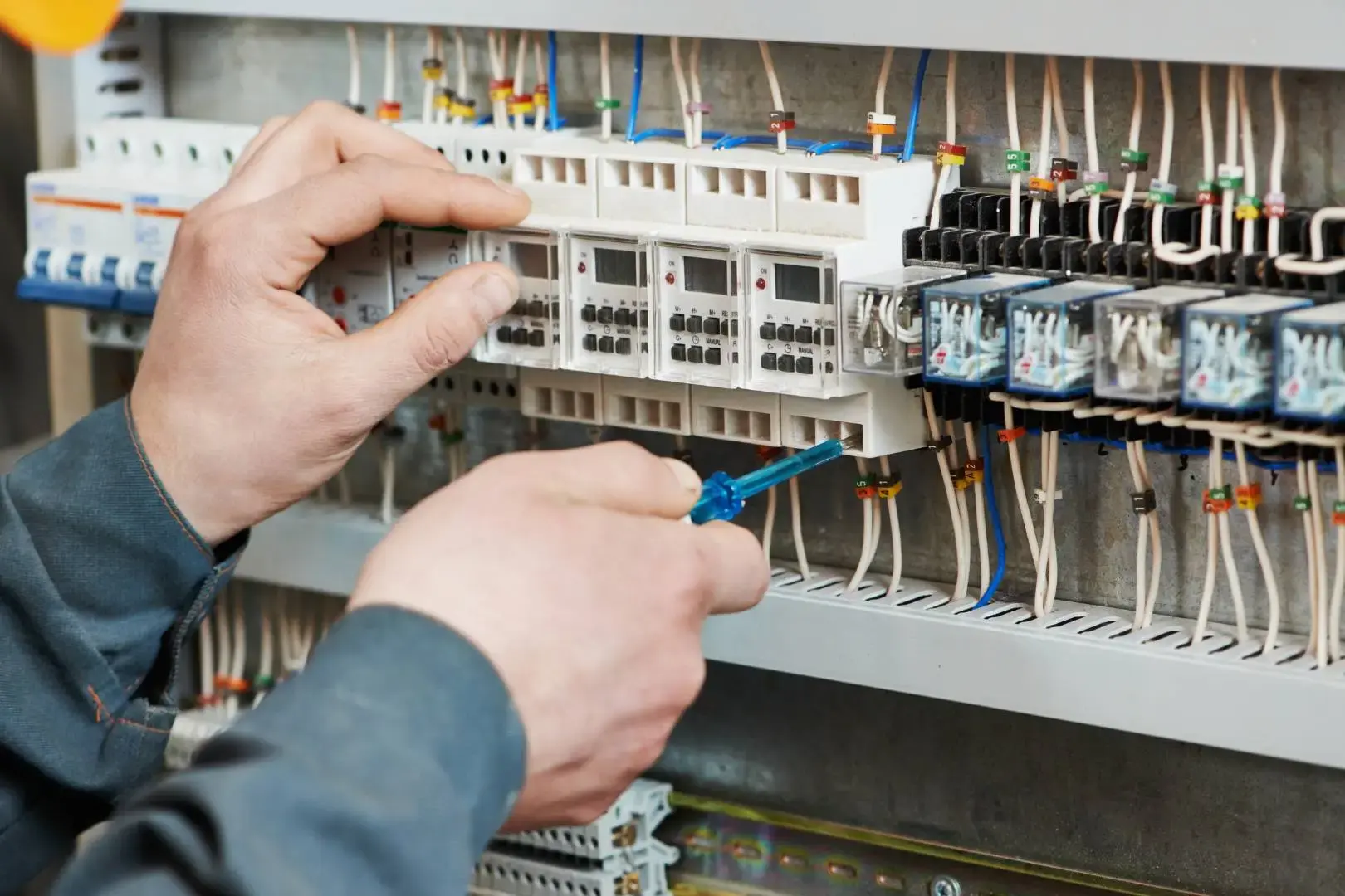 Electrician working inside a switchboard, adjusting and checking terminal connections and wiring within an electrical control panel.