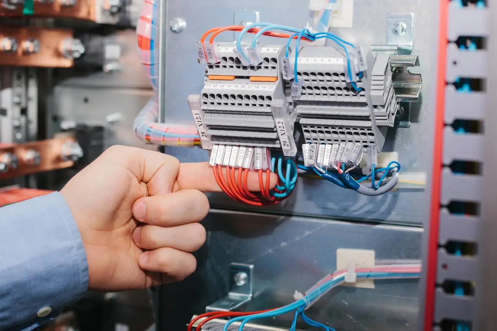 Electrician inspecting and adjusting organised wiring inside an electrical distribution board with labelled terminals.